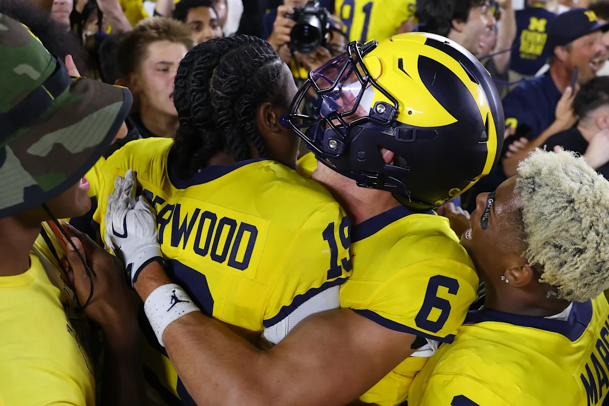 Michigan football players in maize uniforms celebrate amid a crowded sideline after a game