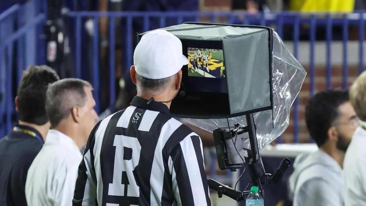 Football official reviews replay footage on a sideline monitor during a game.
