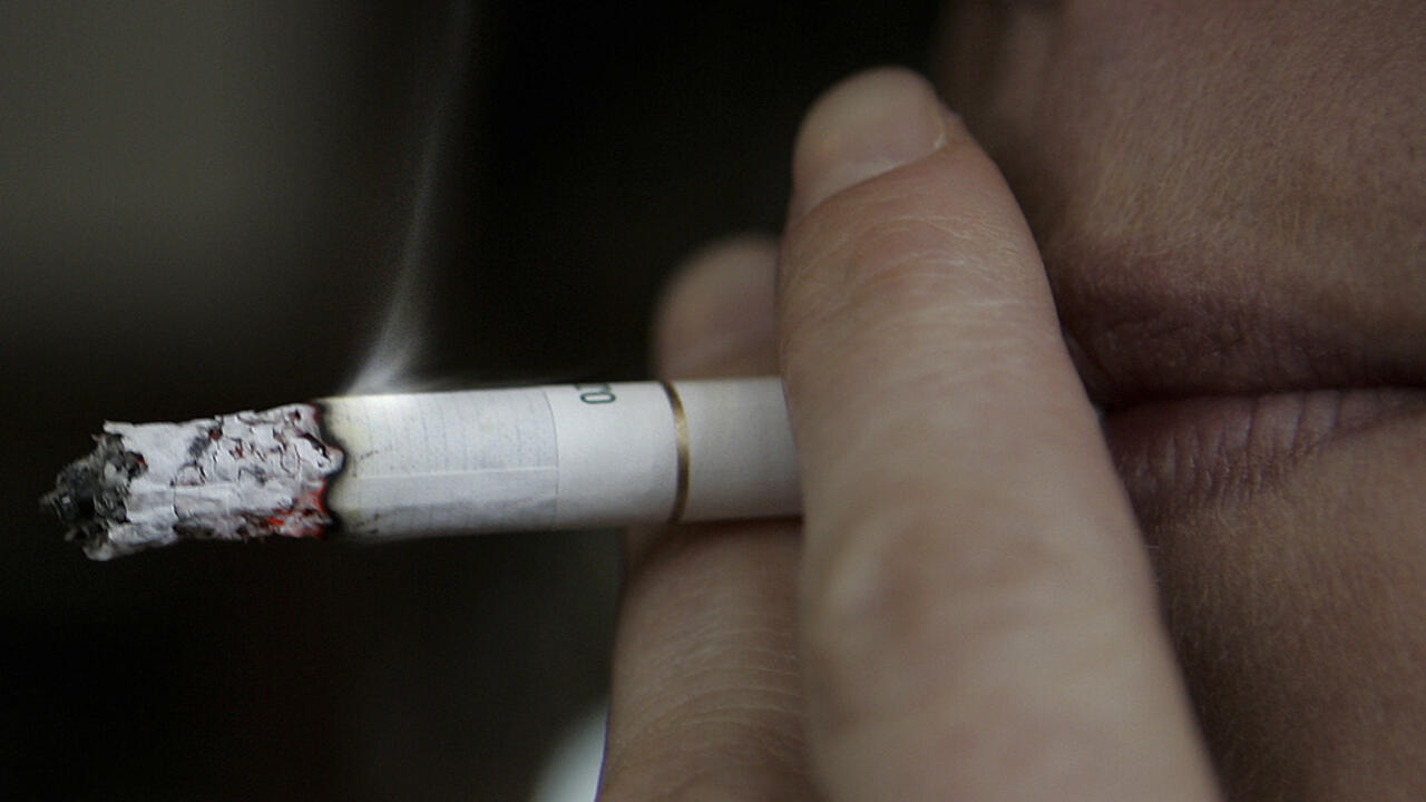 Close-up of a person holding a lit cigarette between their fingers near their lips