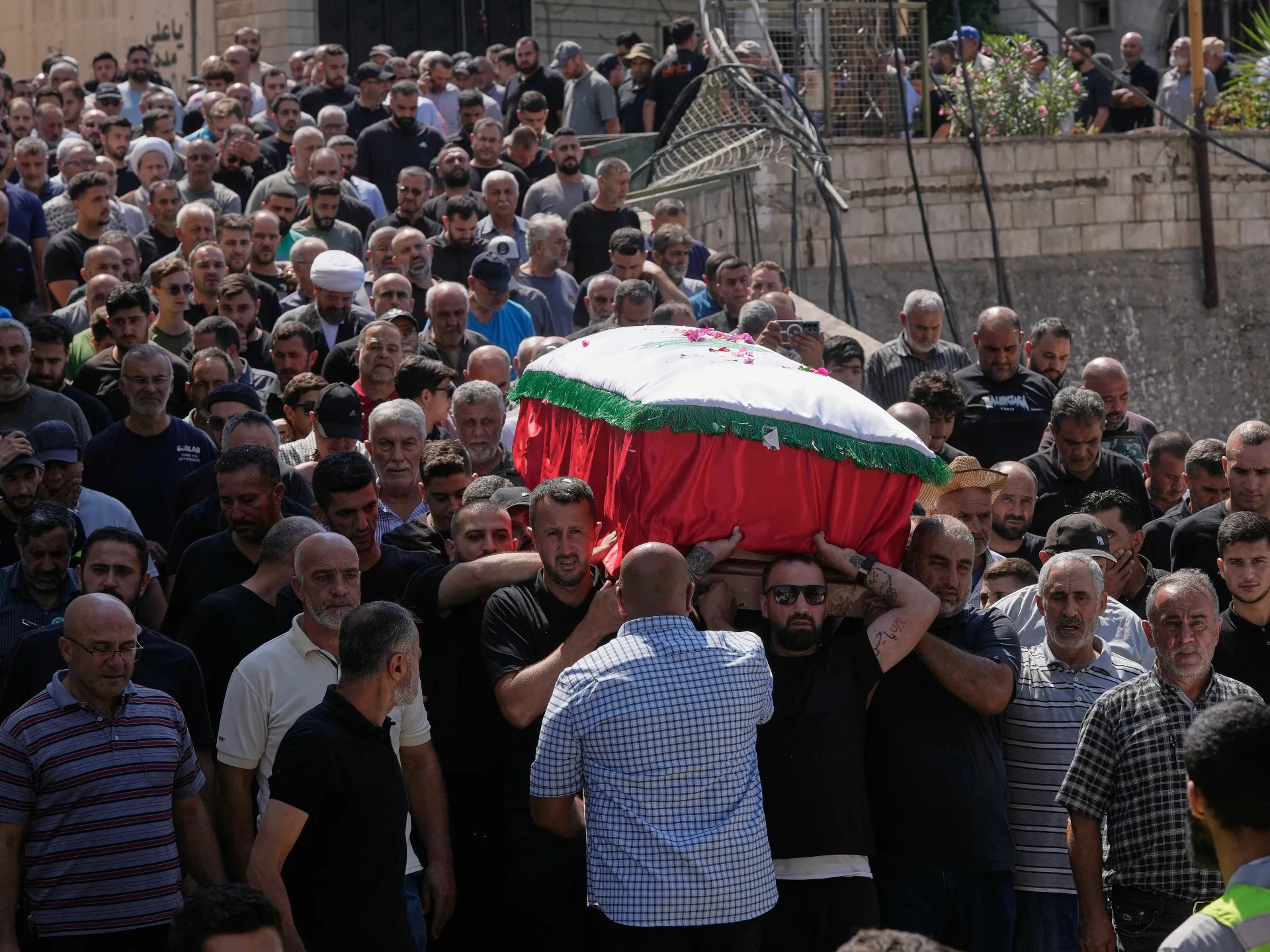 Crowd carries a flower-strewn, red-and-white-covered coffin during a funeral procession.