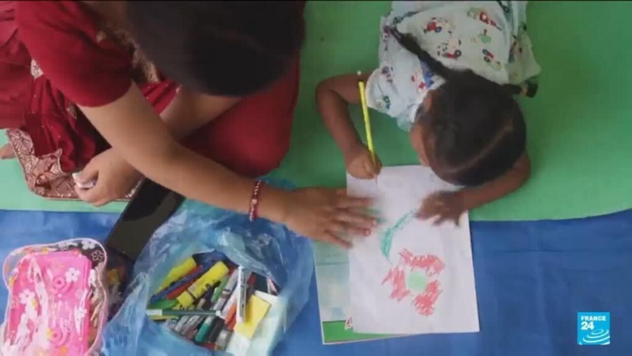 Adult helps a child draw on paper beside a bag of colored pencils