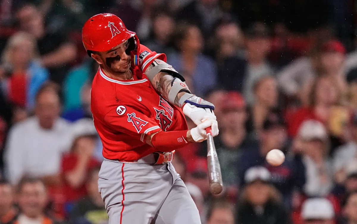 Angels batter in red helmet swings at a pitch as the baseball approaches.