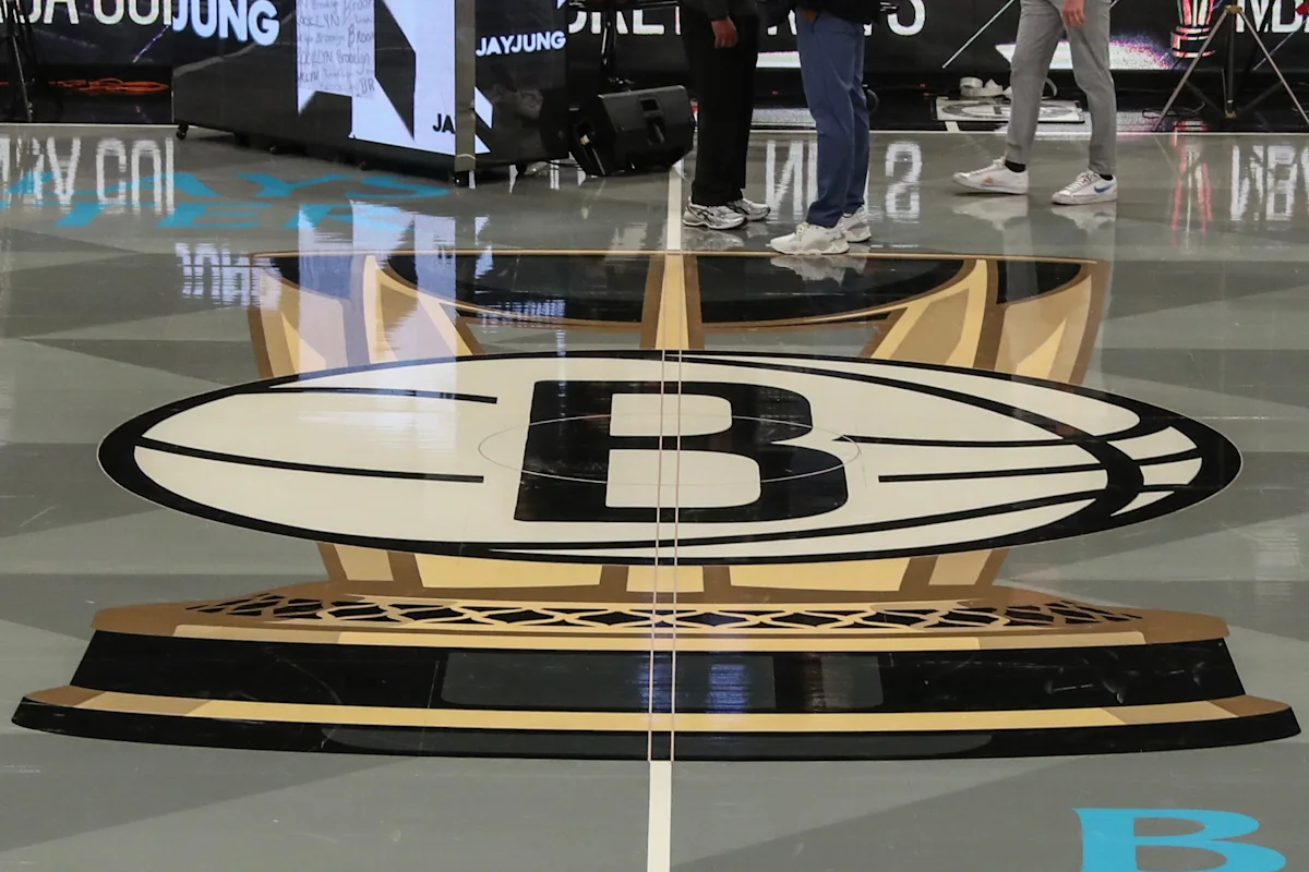 Brooklyn Nets logo displayed on a polished basketball court with people standing in the background