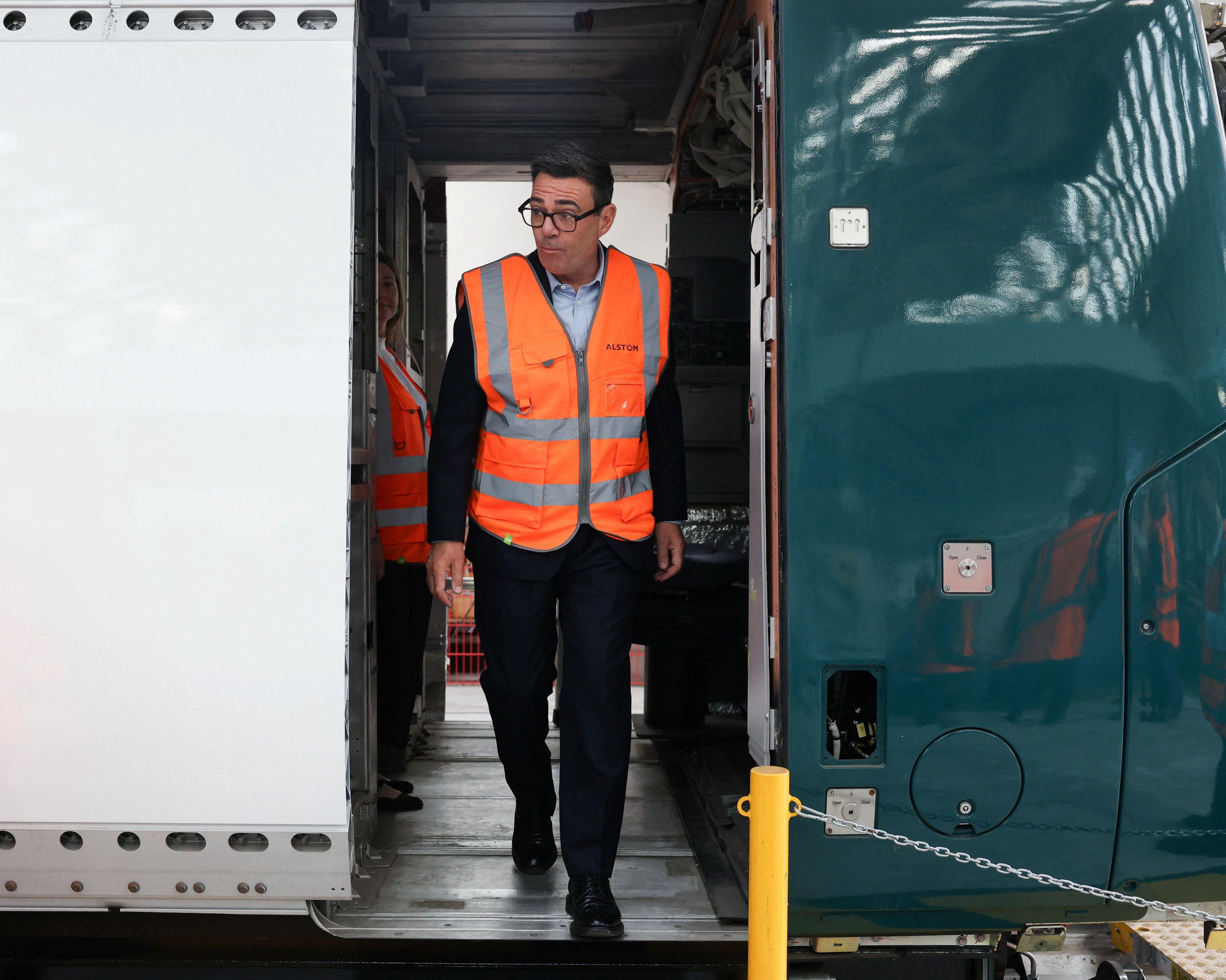 Man in an orange high-visibility vest steps from a train carriage beside an open door.