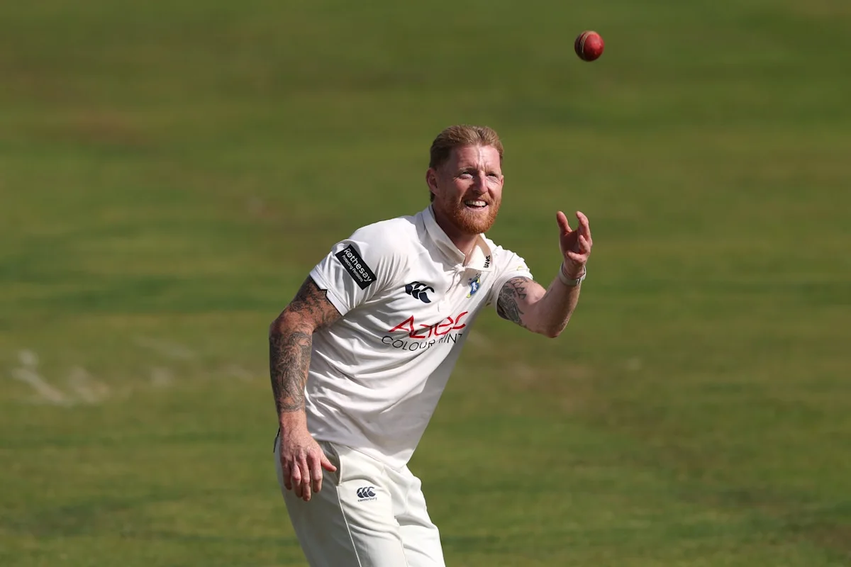 Cricketer in white uniform reaches toward a red ball on a grassy field