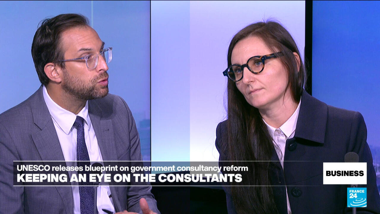 A man and woman in glasses discuss consulting reforms during a televised business interview.