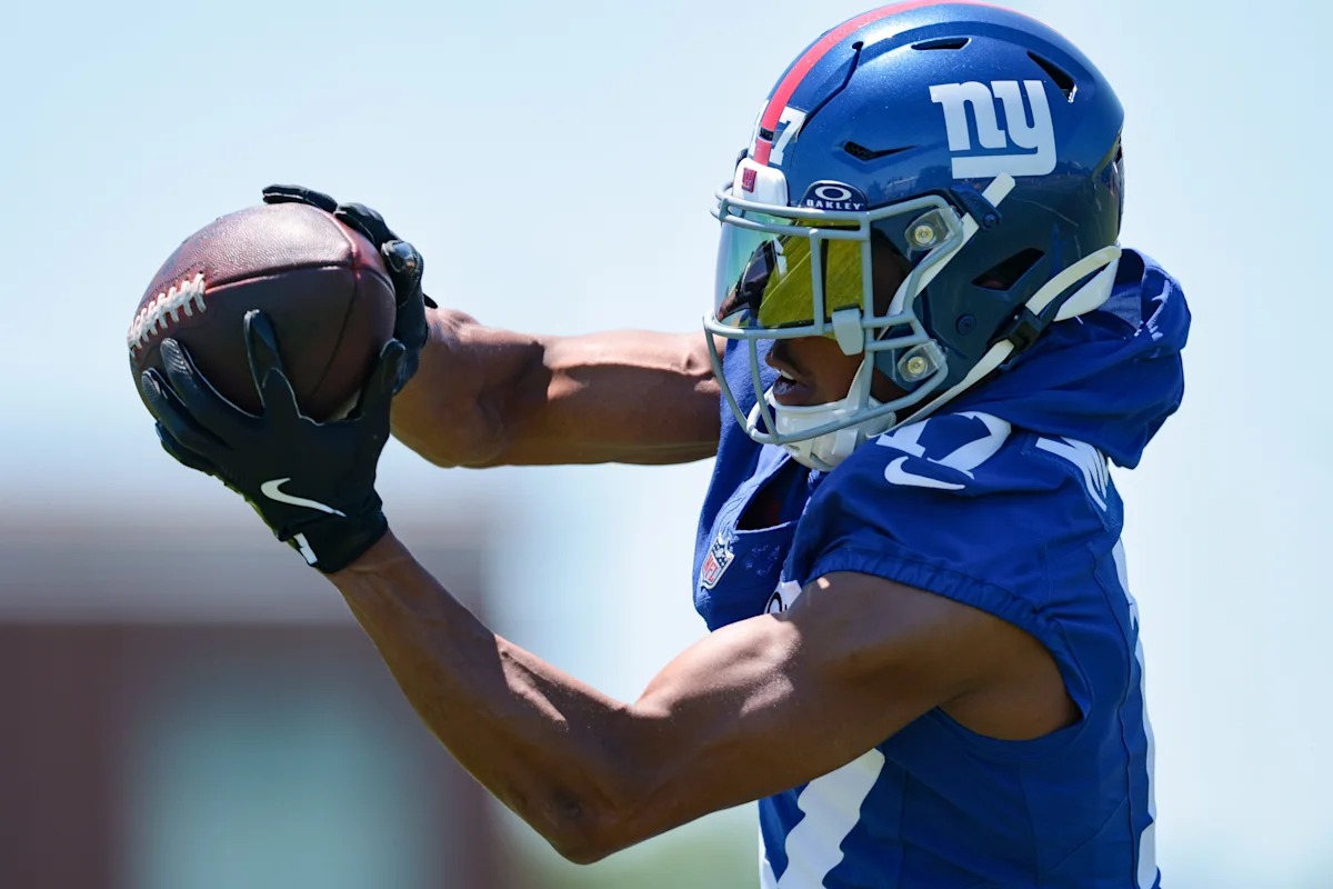 New York Giants football player in blue helmet reaches to catch a football during practice