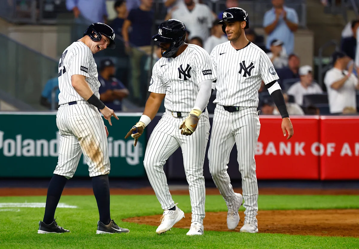Three New York Yankees players in pinstriped uniforms walk together on the baseball field.