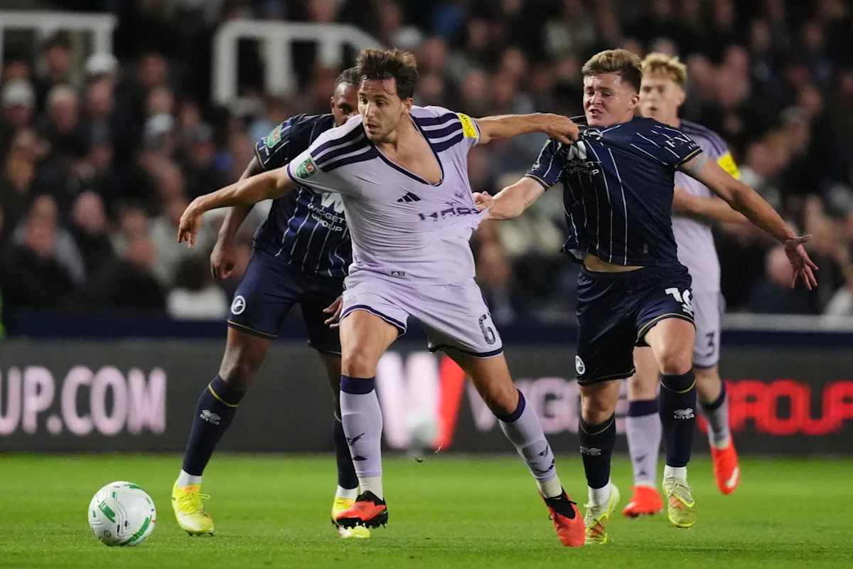 Footballers challenge for the ball during a competitive match under stadium lights.