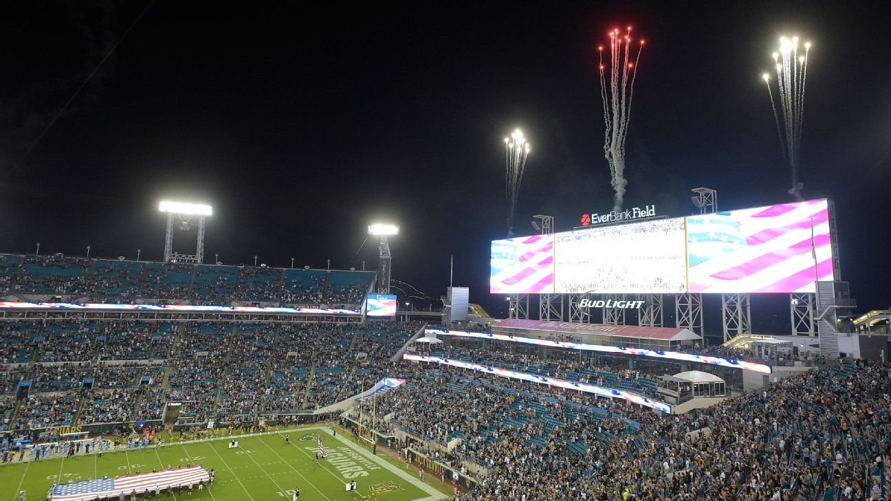 Nighttime football stadium with illuminated videoboard, fireworks, packed stands, and an American flag on the field