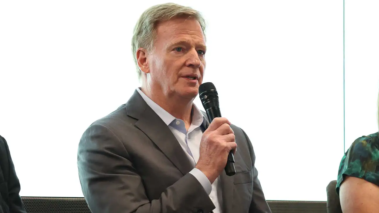 A gray-haired man in a suit speaks into a handheld microphone at an event.