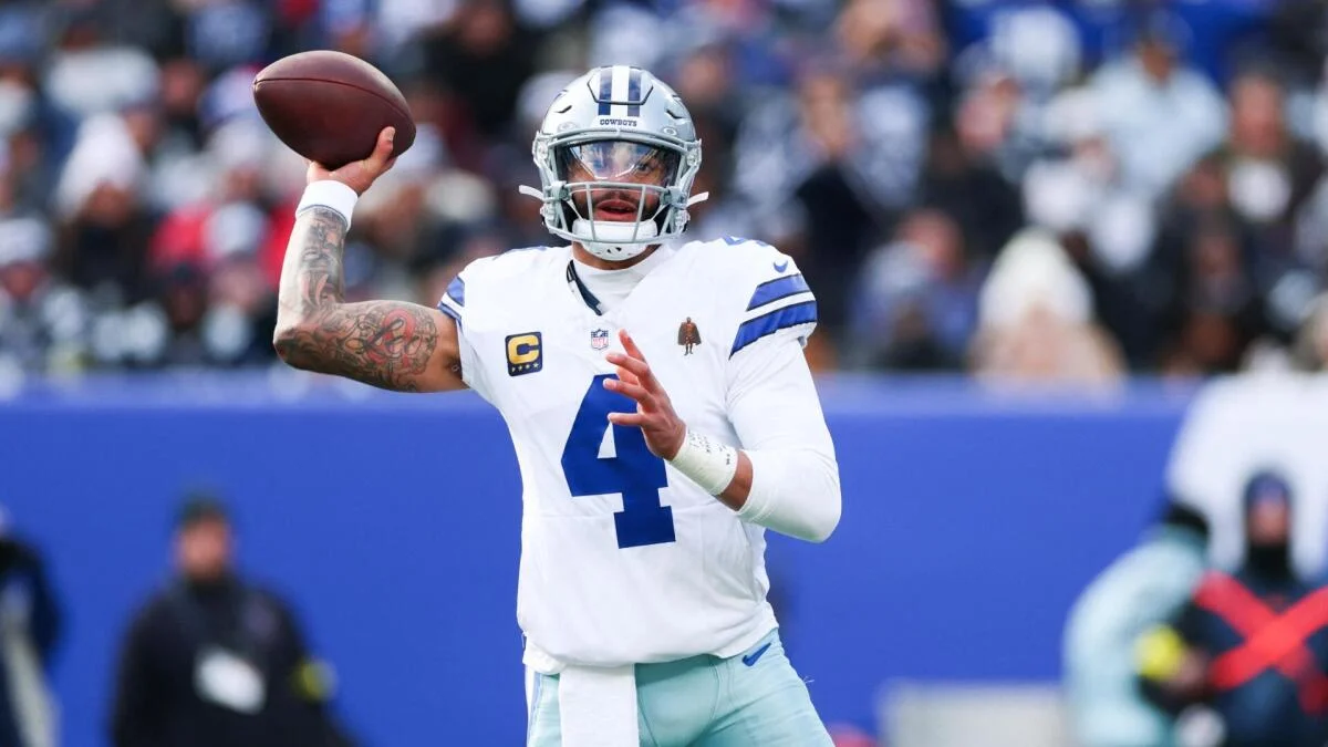 Dallas Cowboys quarterback in uniform prepares to throw a football during an NFL game.