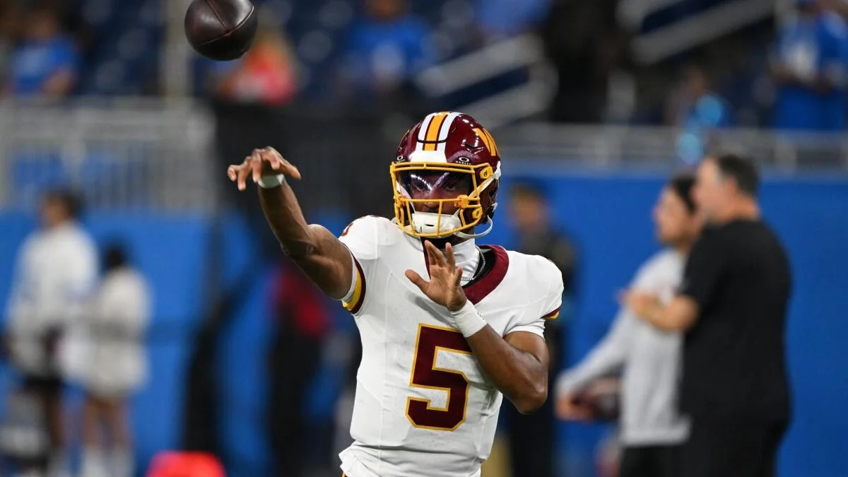 Quarterback in a burgundy helmet and white jersey throws a football during an NFL game.
