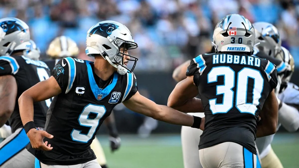 Carolina Panthers players in black uniforms gather on the field, with number 9 facing number 30.