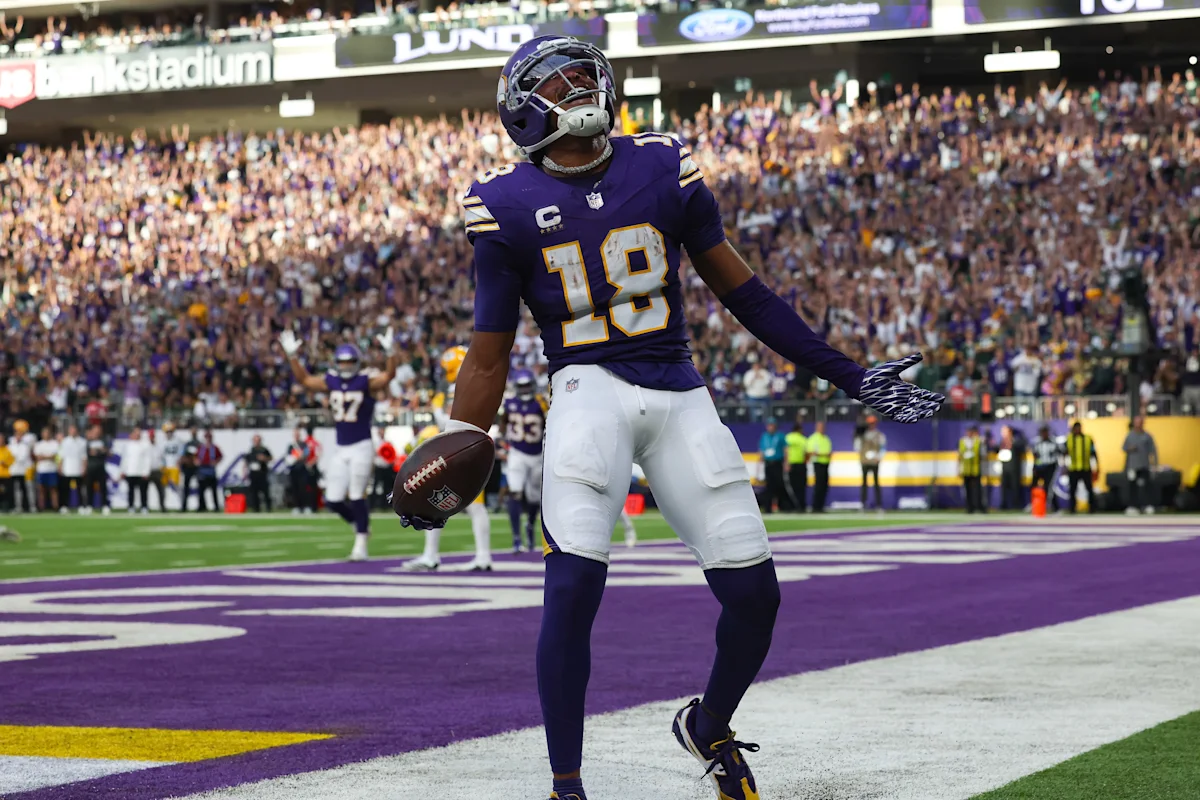 Football player in purple uniform celebrates with the ball in a stadium end zone.