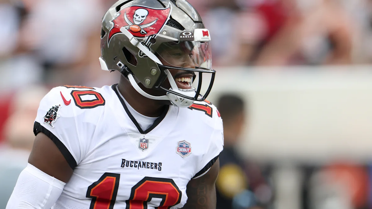 A Tampa Bay Buccaneers player in a white number 10 jersey smiles while wearing a team helmet.