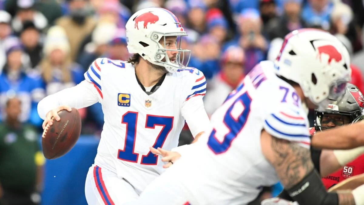 Buffalo quarterback in a white number 17 jersey holds the football as teammates block nearby.
