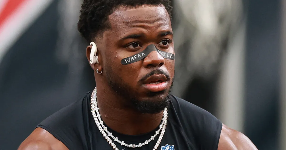 A football player wearing black eye paint reading “WAFAA AKILA,” earbuds, and layered necklaces.