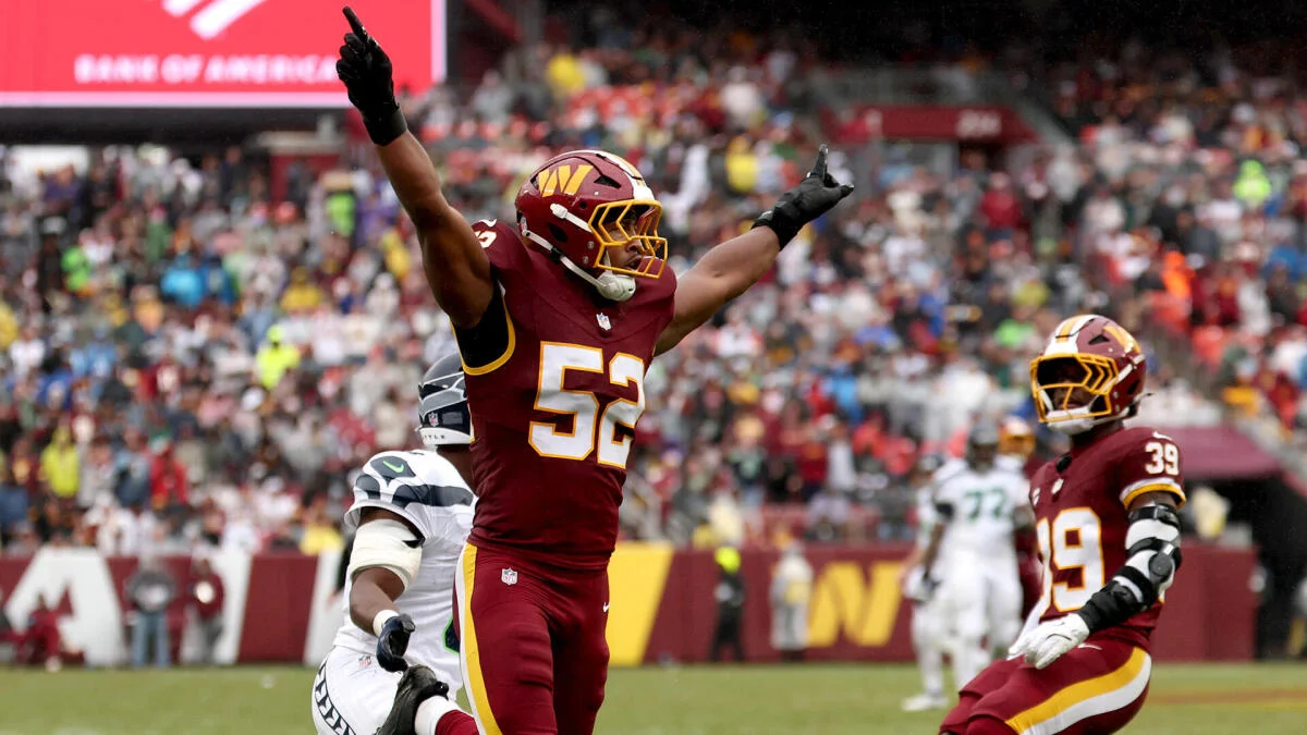 Washington player in burgundy jersey raises both arms as teammate celebrates during an NFL game.