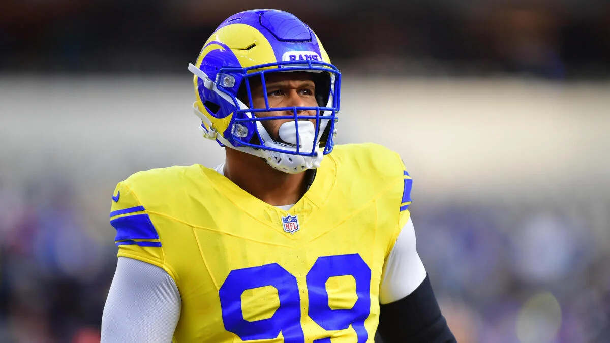Football player wearing a yellow jersey and blue face mask against a blurred stadium background