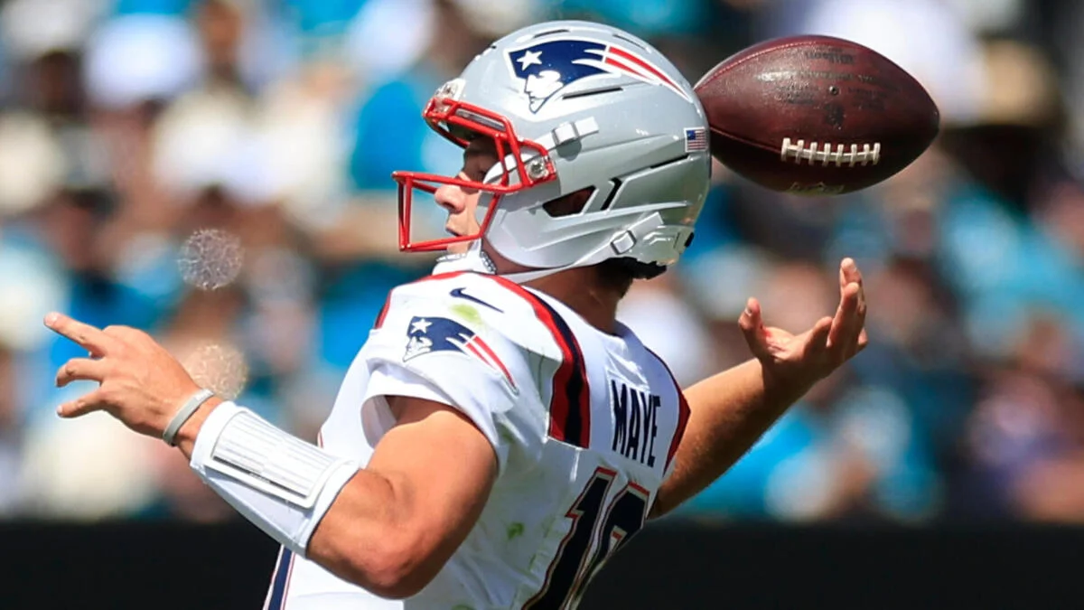 New England Patriots quarterback in a white uniform throws a football during a game.