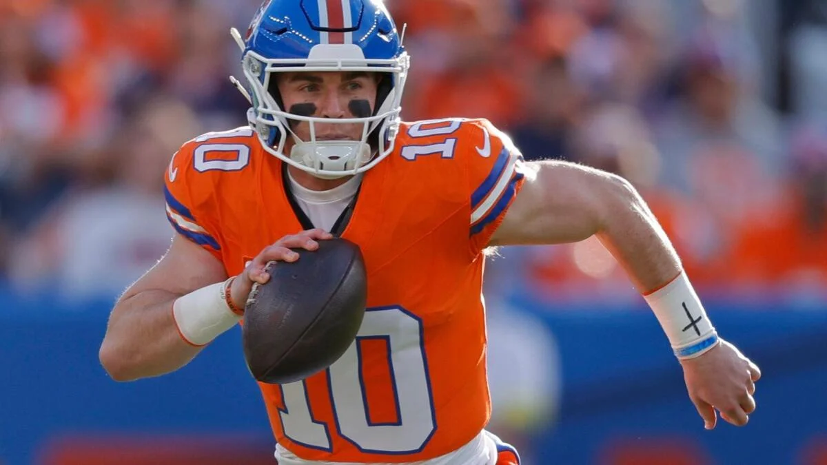 A Denver Broncos player in an orange uniform runs with the football during a game.