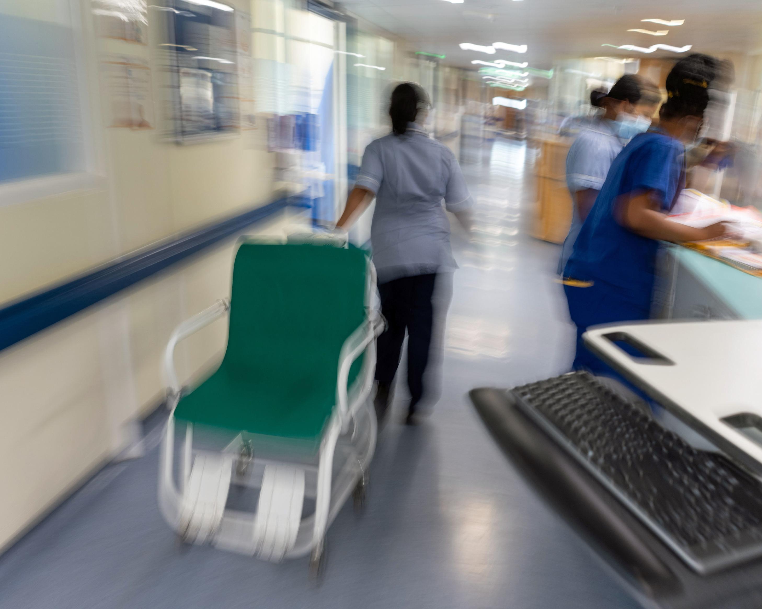 Blurred hospital corridor with healthcare workers moving beside a green trolley and medical equipment.