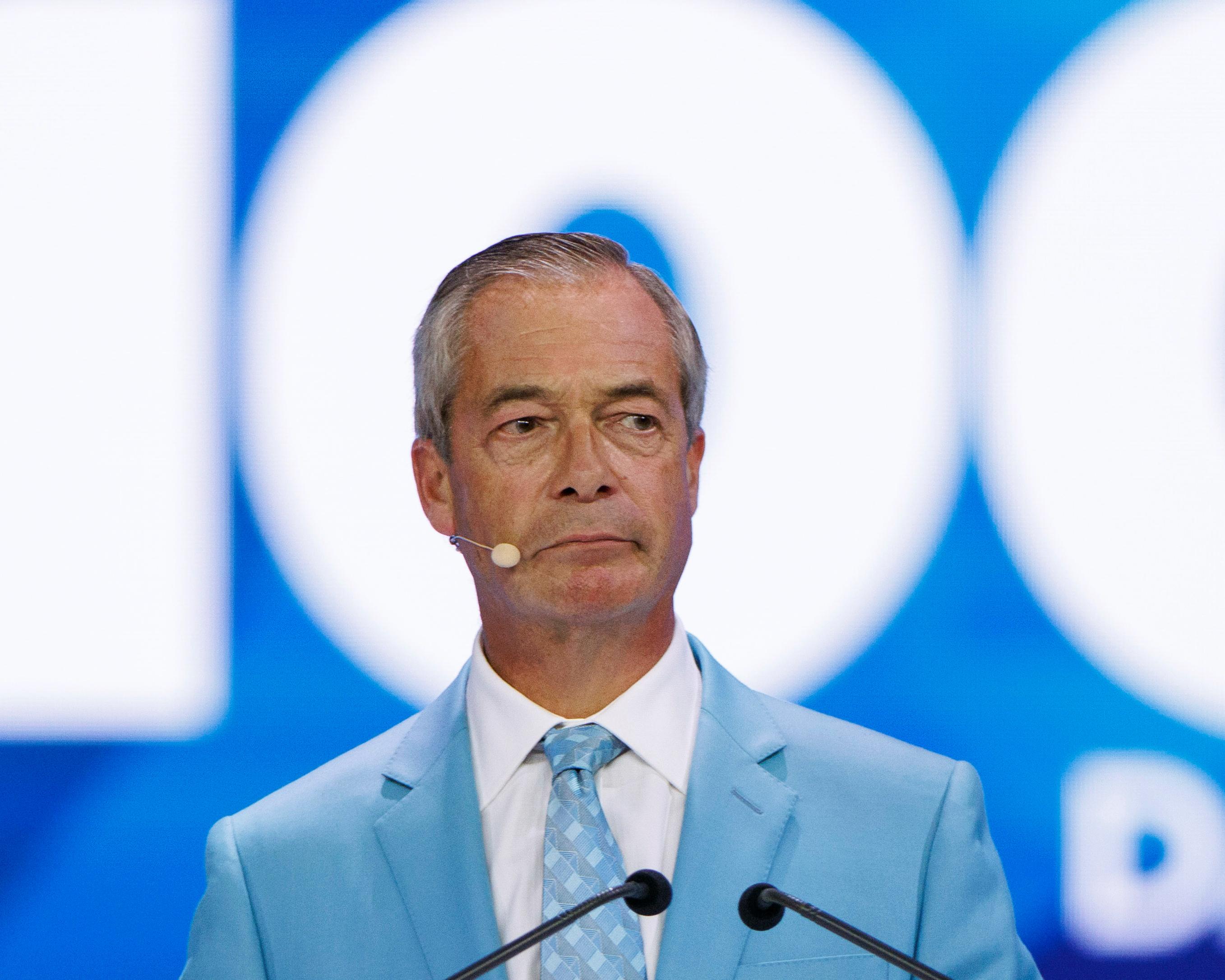 Man in pale blue suit and tie speaking at a podium with microphones