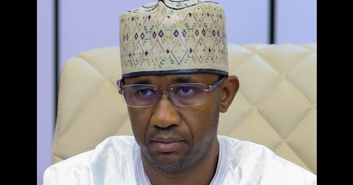 Man wearing an embroidered traditional cap and glasses seated in a cream-colored chair