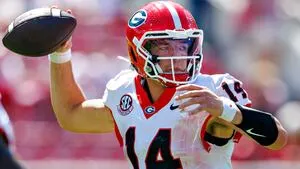 Georgia football player in a red helmet throws a pass during a game.