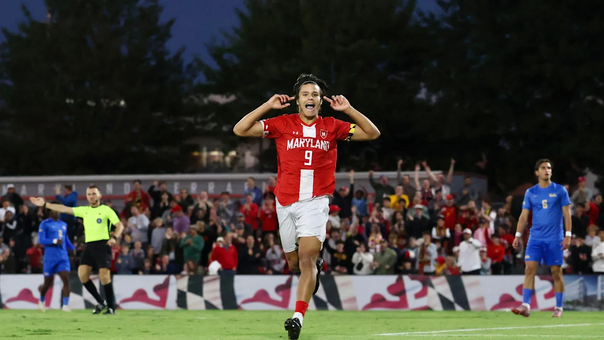 Maryland player in a red number 9 jersey celebrates on the field as opponents and a referee look on.