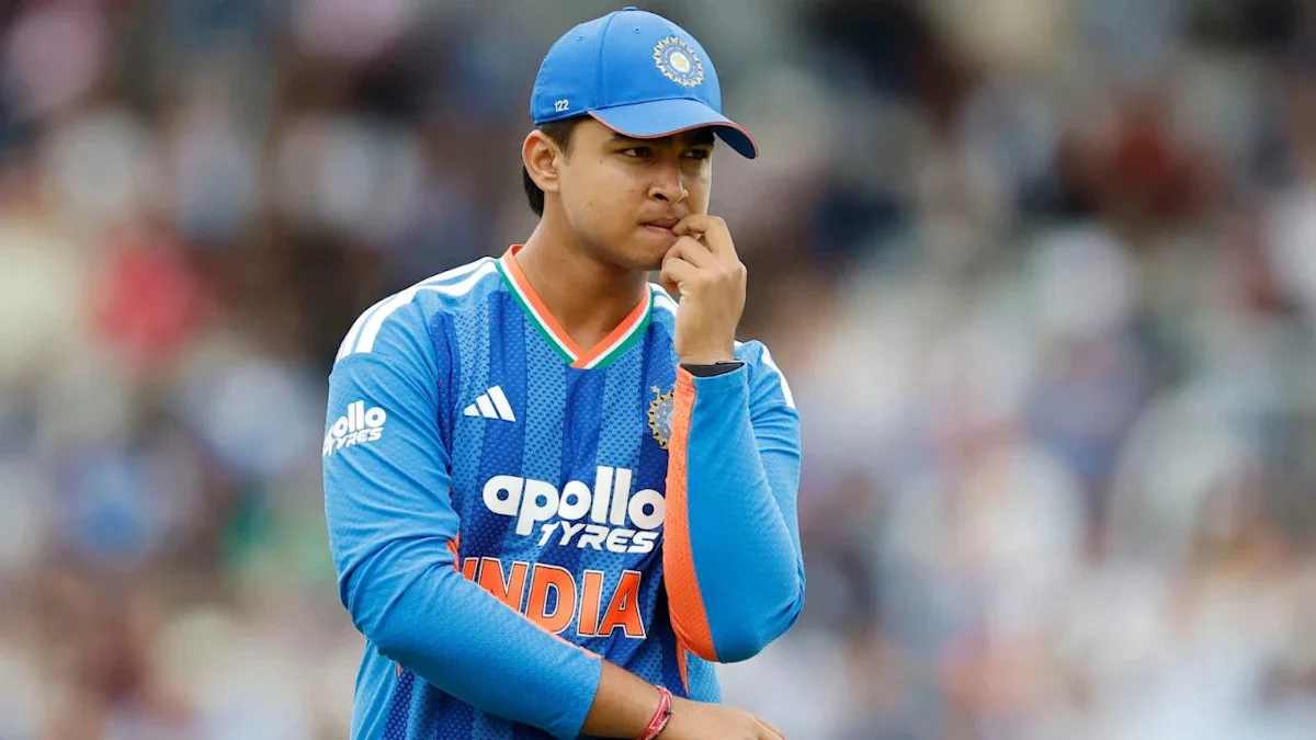 A young cricketer in India’s blue kit stands with arms crossed, touching his lips.