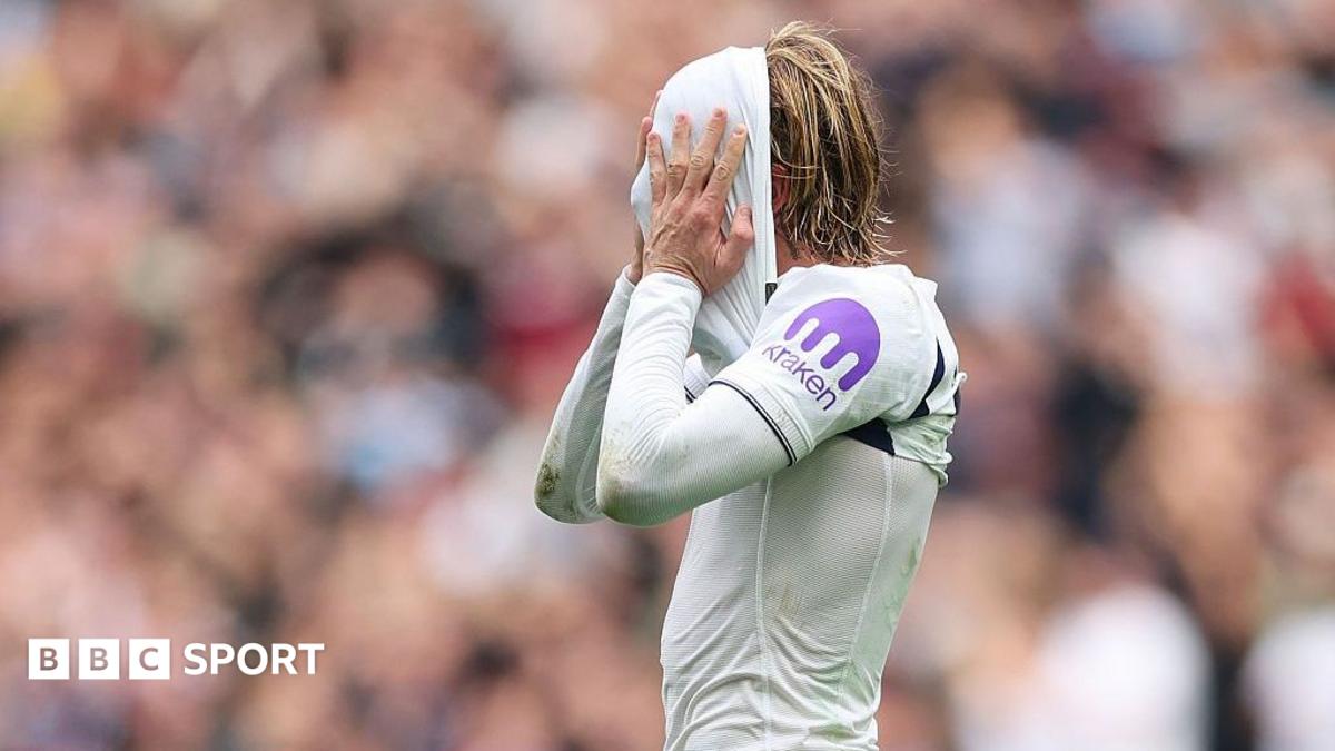 Footballer in a white kit covers their face with a towel during a match.