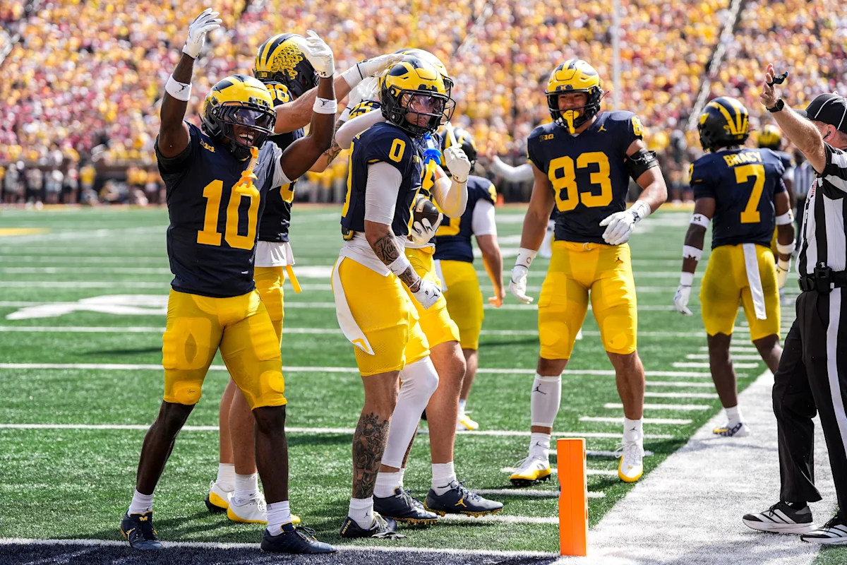 Michigan football players celebrate on the sideline during a sunny game at Michigan Stadium.