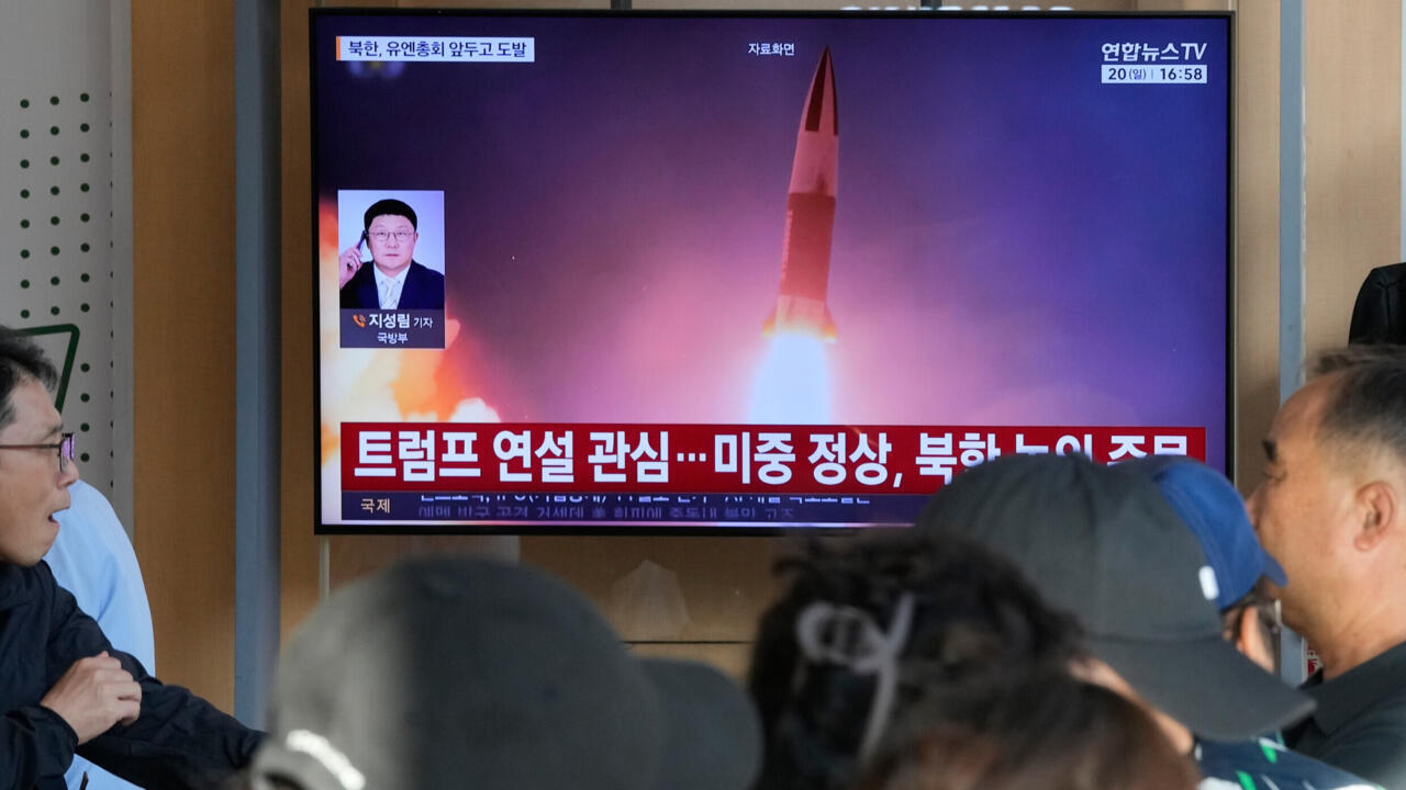 Television displays a missile launch graphic while several people watch in the foreground.