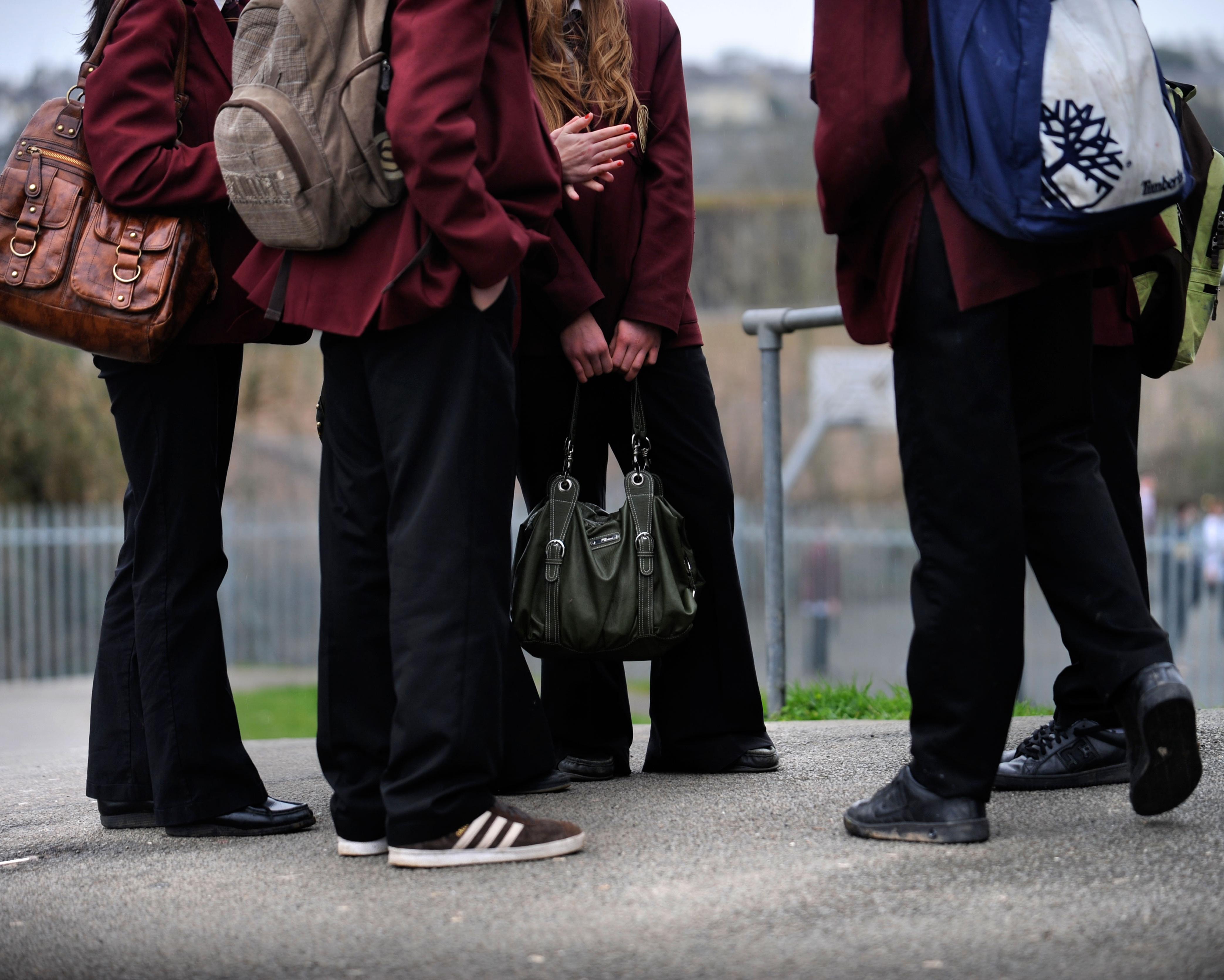 Schoolgirls in burgundy blazers and black trousers carrying backpacks and handbags outdoors