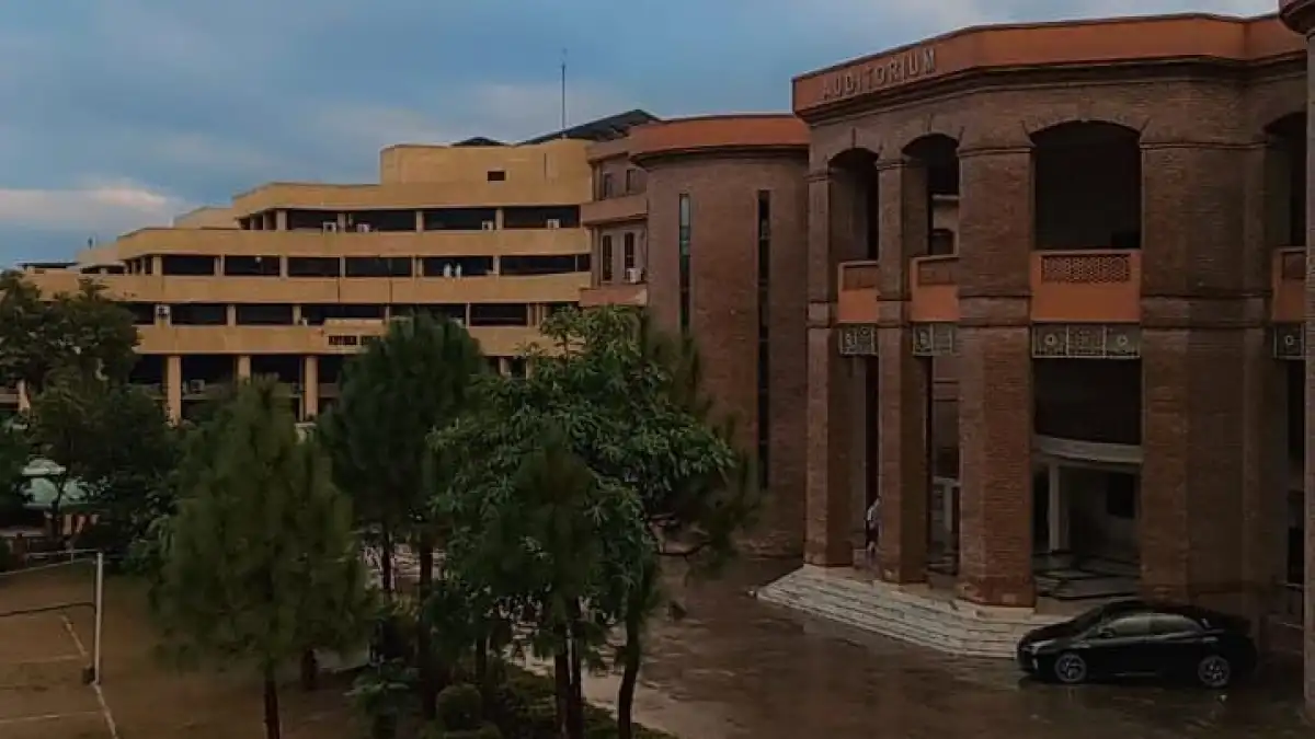Exterior of a brick auditorium building beside a modern tan complex and tree-lined courtyard.