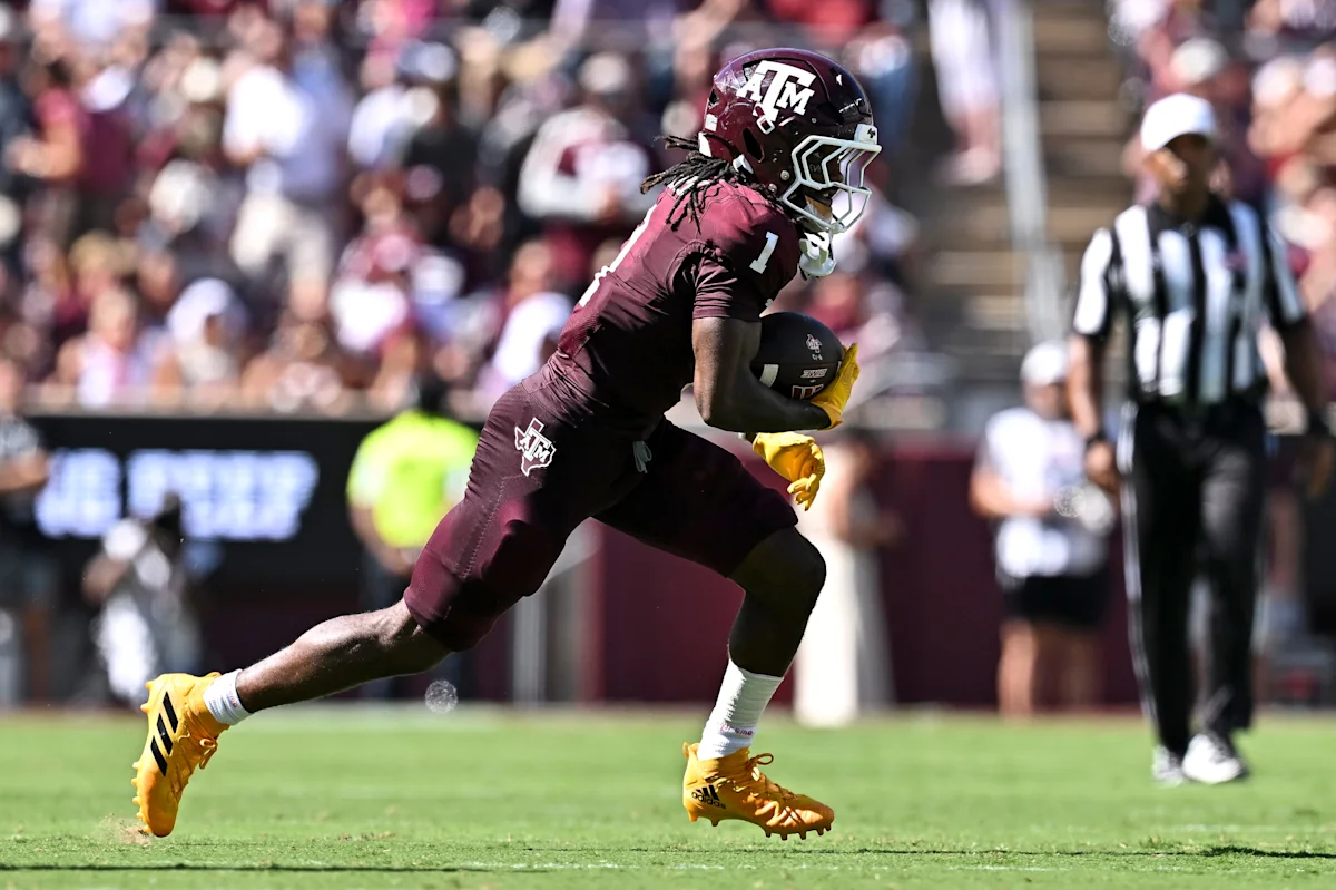 Texas A&M football player in maroon runs with the ball during a game.