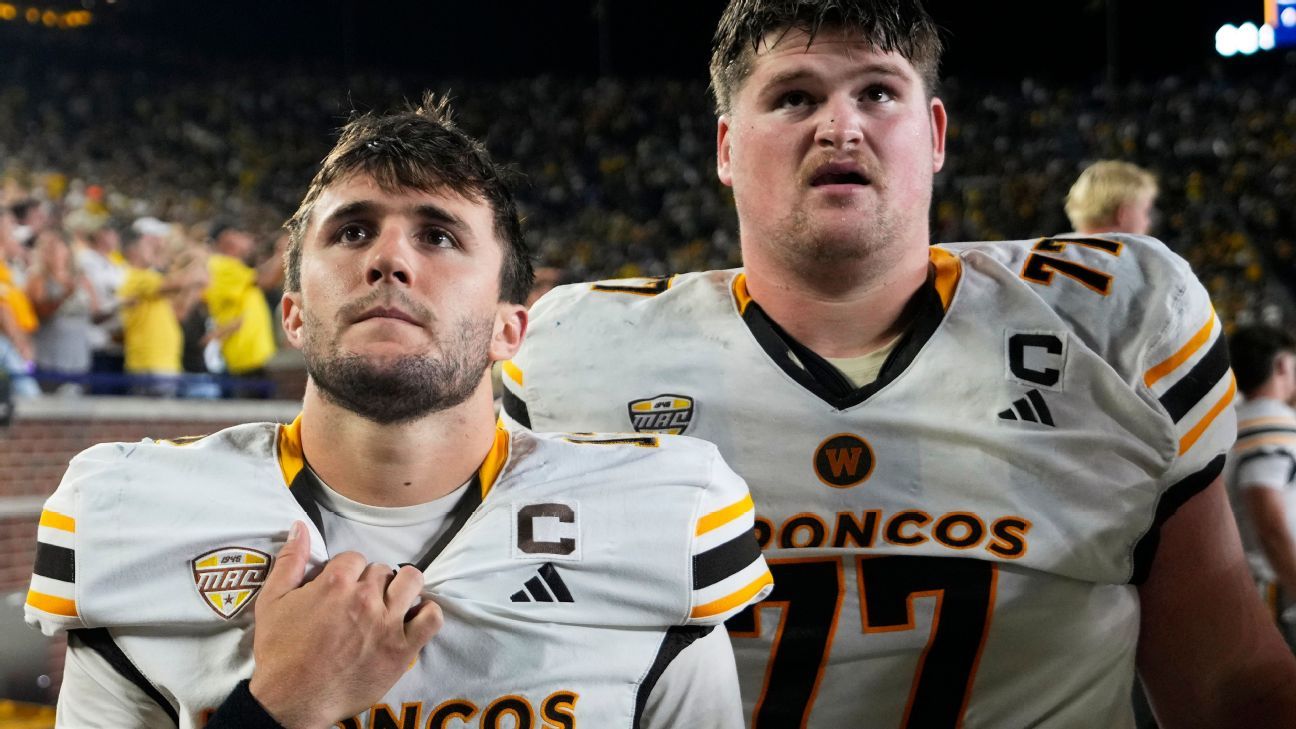 Two football players in white Broncos jerseys stand together on a field after a game.