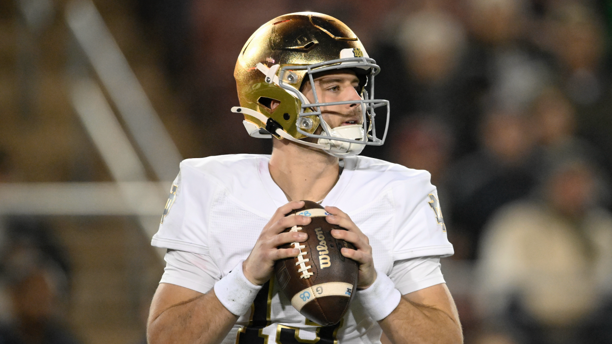 Notre Dame quarterback in a gold helmet grips the football before a play.
