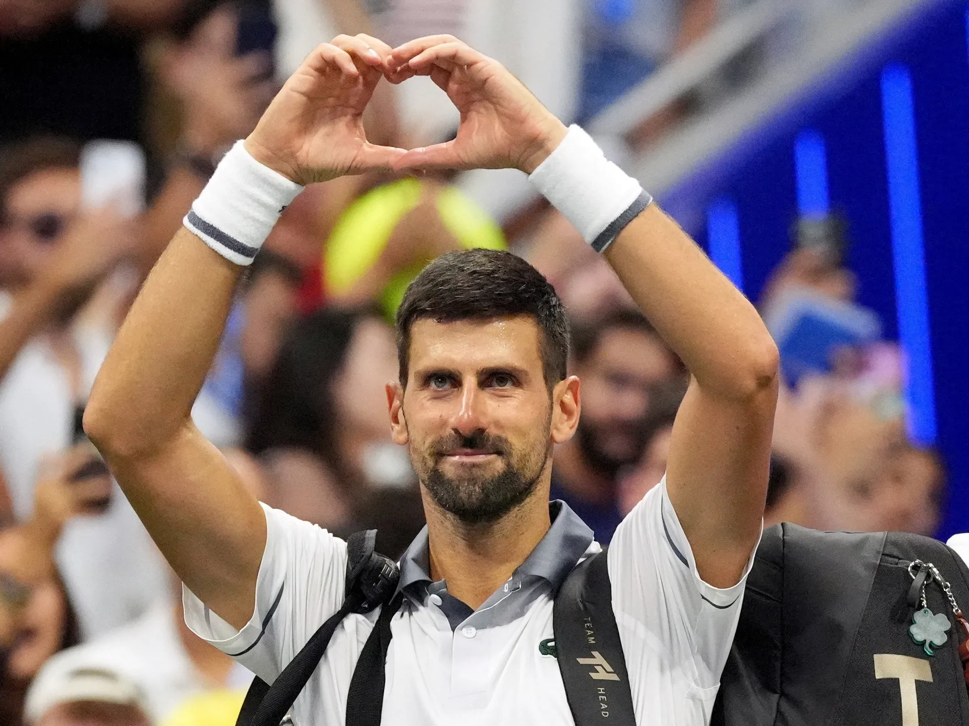 Tennis player raises his arms and forms a heart shape with his hands before a crowd.
