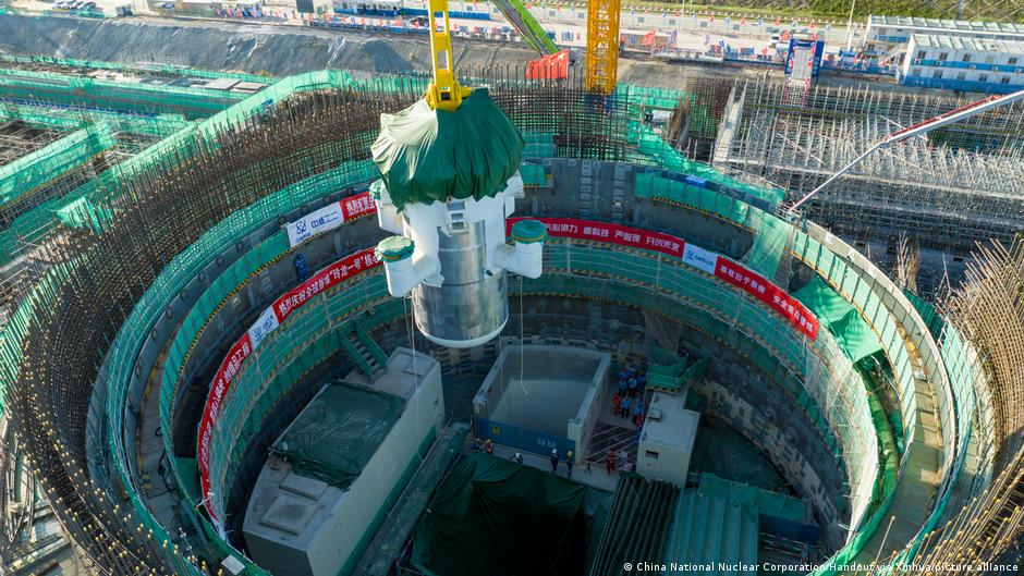 Construction workers assemble a large cylindrical structure inside a circular, reinforced construction site.