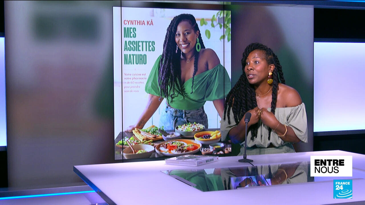 Nutrition expert speaking at a studio desk beside a screen showing a healthy eating magazine cover.