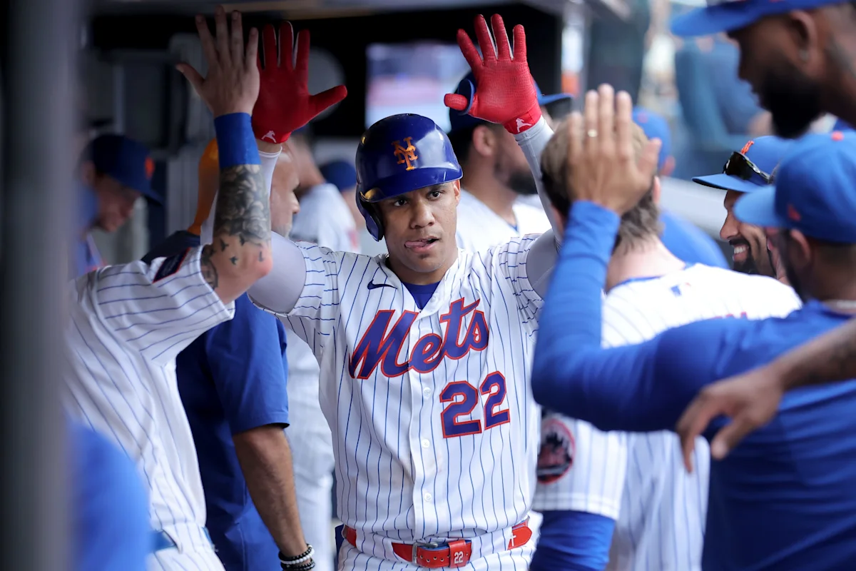 Mets player wearing number 22 raises his hands as teammates celebrate around him in the dugout