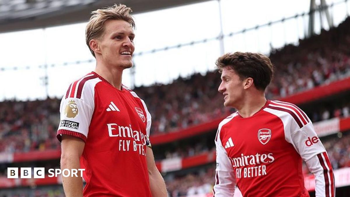 Two Arsenal players in red-and-white shirts stand on the pitch during a match.