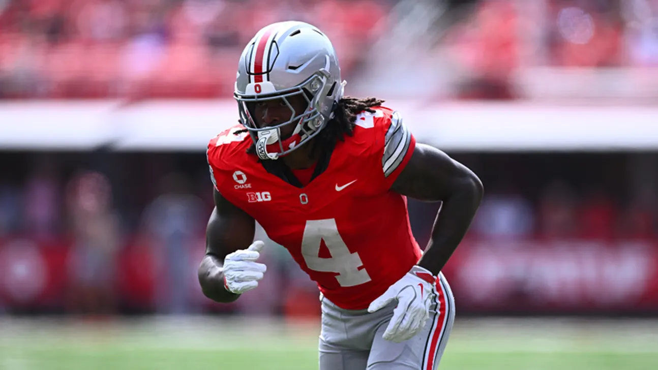 Football player in a red number 4 jersey and silver helmet leans forward on the field.