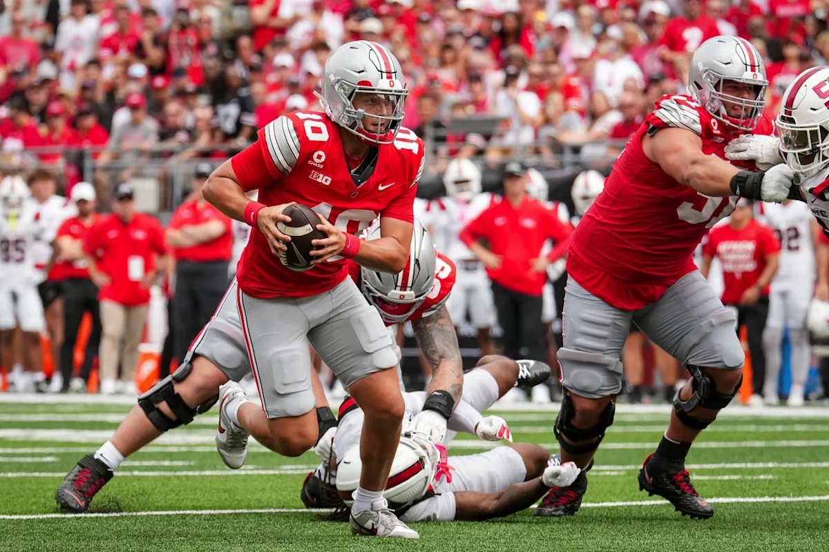Ohio State football player carries the ball as teammates block during a game