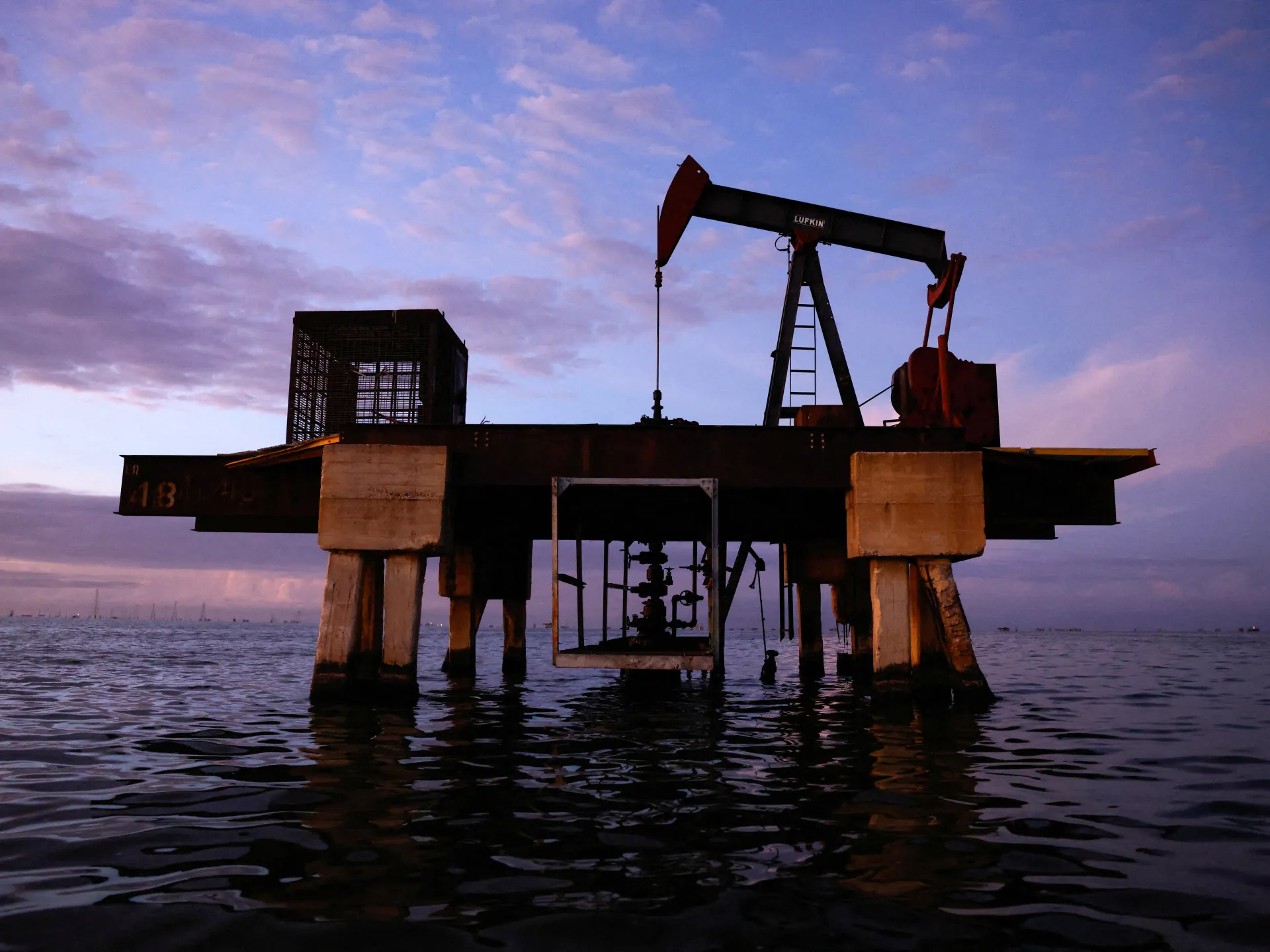 Oil pumpjack standing over water beneath a purple and blue dusk sky
