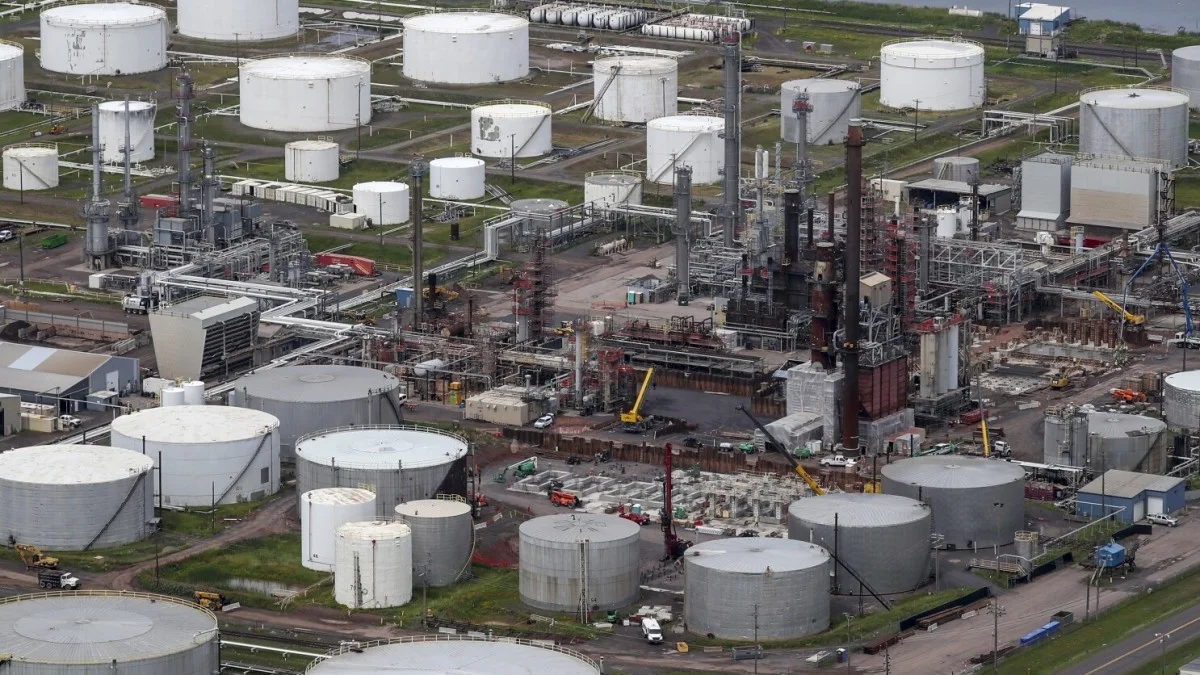Aerial view of an oil refinery complex with storage tanks, processing towers, pipes, and construction equipment.