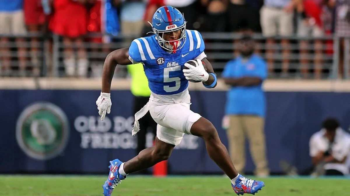 Ole Miss player in a blue number five uniform runs with the football during a game.